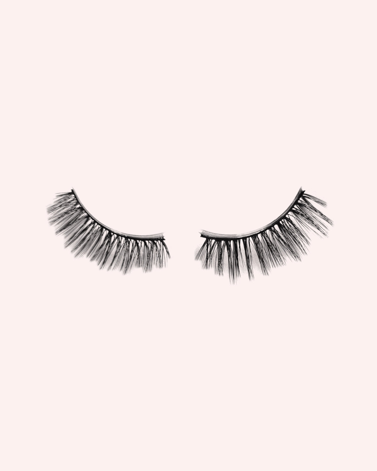 Eén paar Love Me halve wimpers van By Dash Beauty op een lichtroze achtergrond