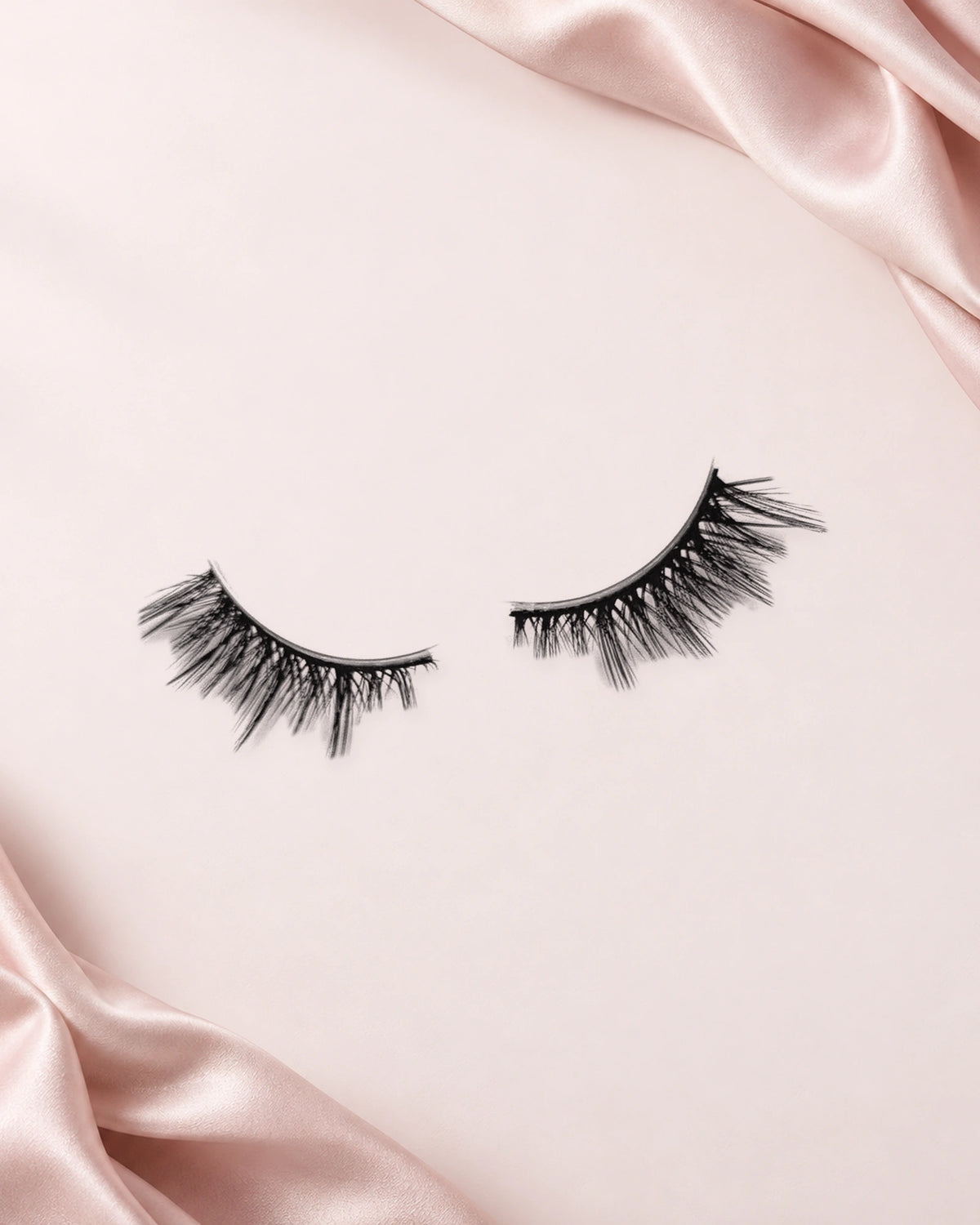 Obsessed halve wimpers van By Dash Beauty op een lichtroze achtergrond met satijn