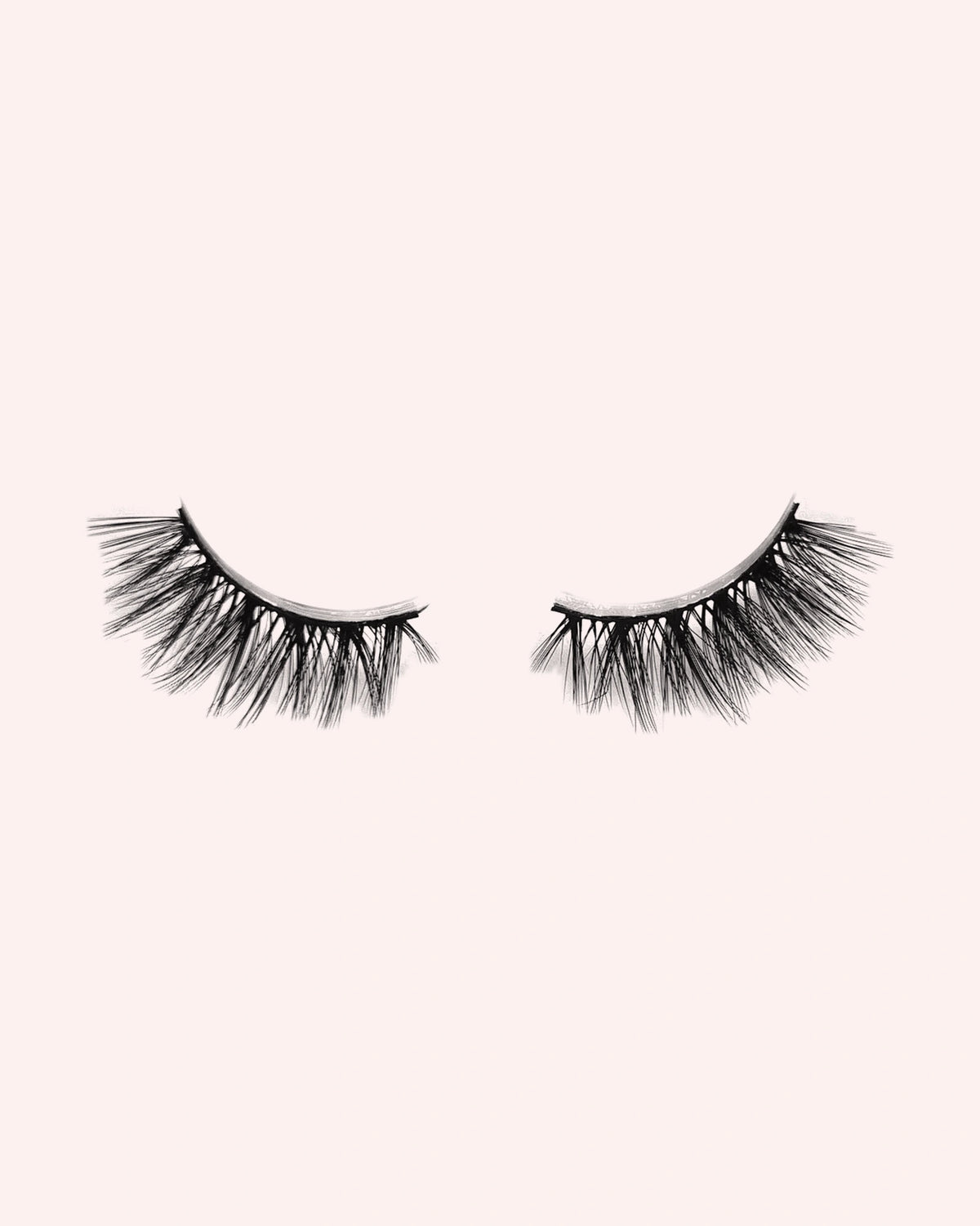 Eén paar Heartbreaker halve wimpers van By Dash Beauty op een lichtroze achtergrond
